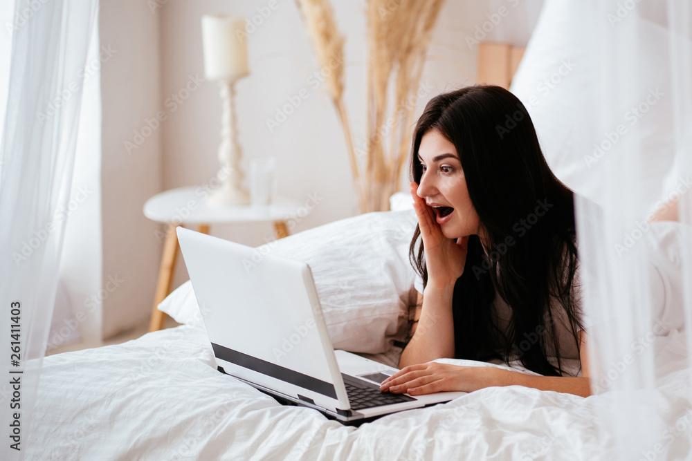 Pretty woman shopping online. Young excited girl using laptop in bedroom. Achievement, freelance, winning, sale success concept Pretty woman shopping online. Young excited girl using laptop in bedroom. Achievement, freelance, winning, sale success concept