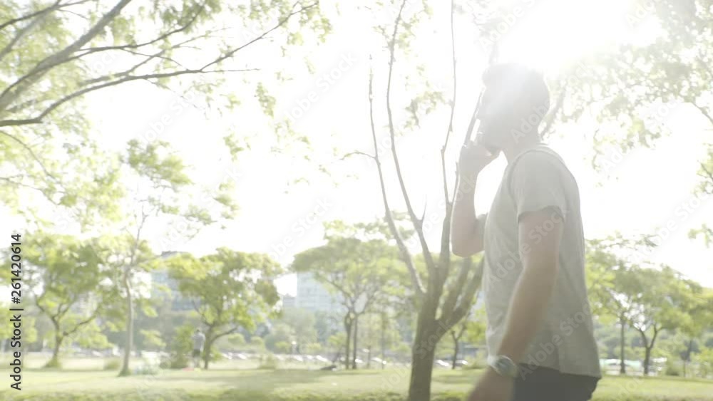 Tracking shot of young man talking on smartphone while walking in park Tracking shot of young man talking on smartphone while walking in park