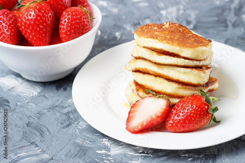 Pancakes on a plate and strawberries on a gray background