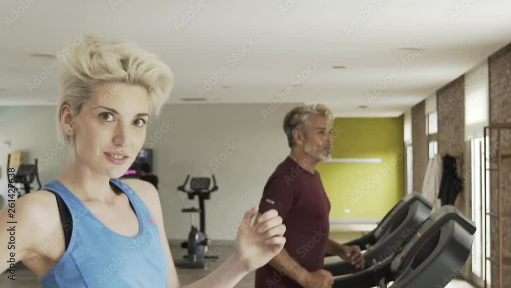 Medium shot of mature man and young woman exercising on treadmill in gym Medium shot of mature man and young woman exercising on treadmill in gym