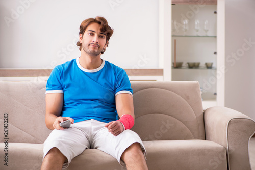Young man with injured arm sitting on the sofa 