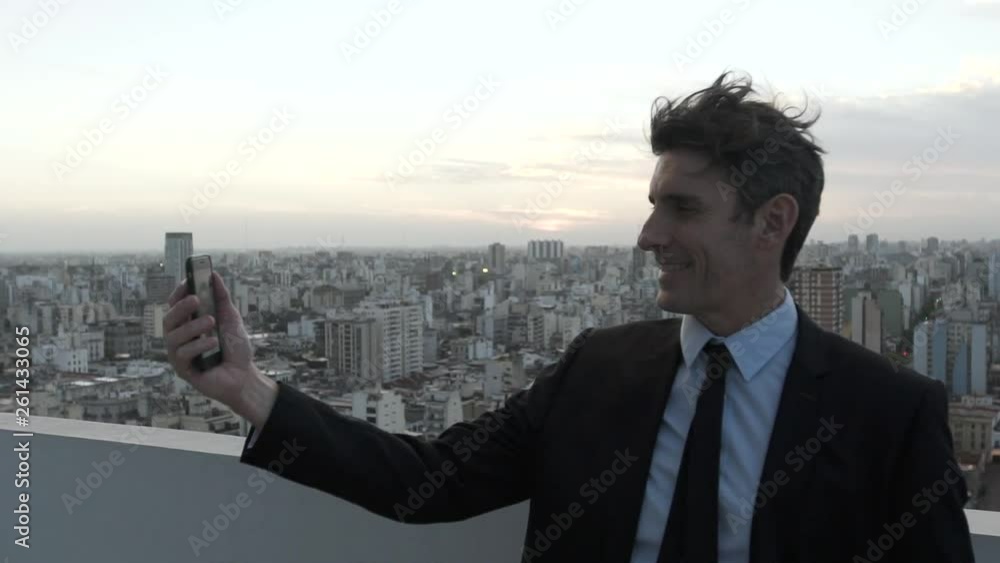 Medium shot of smiling mature businessman having a video call on smartphone while standing on terrace Medium shot of smiling mature businessman having a video call on smartphone while standing on terrace
