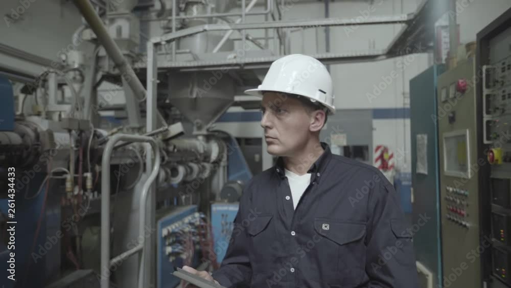 Medium shot of engineer using digital tablet and examining machinery in factory Medium shot of engineer using digital tablet and examining machinery in factory
