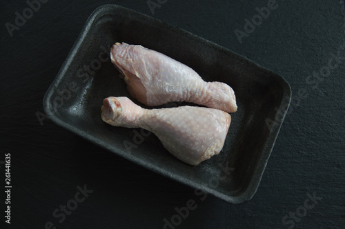 Two raw chicken legs lie in a plastic container on a black background. Thaw and cook chicken legs.
