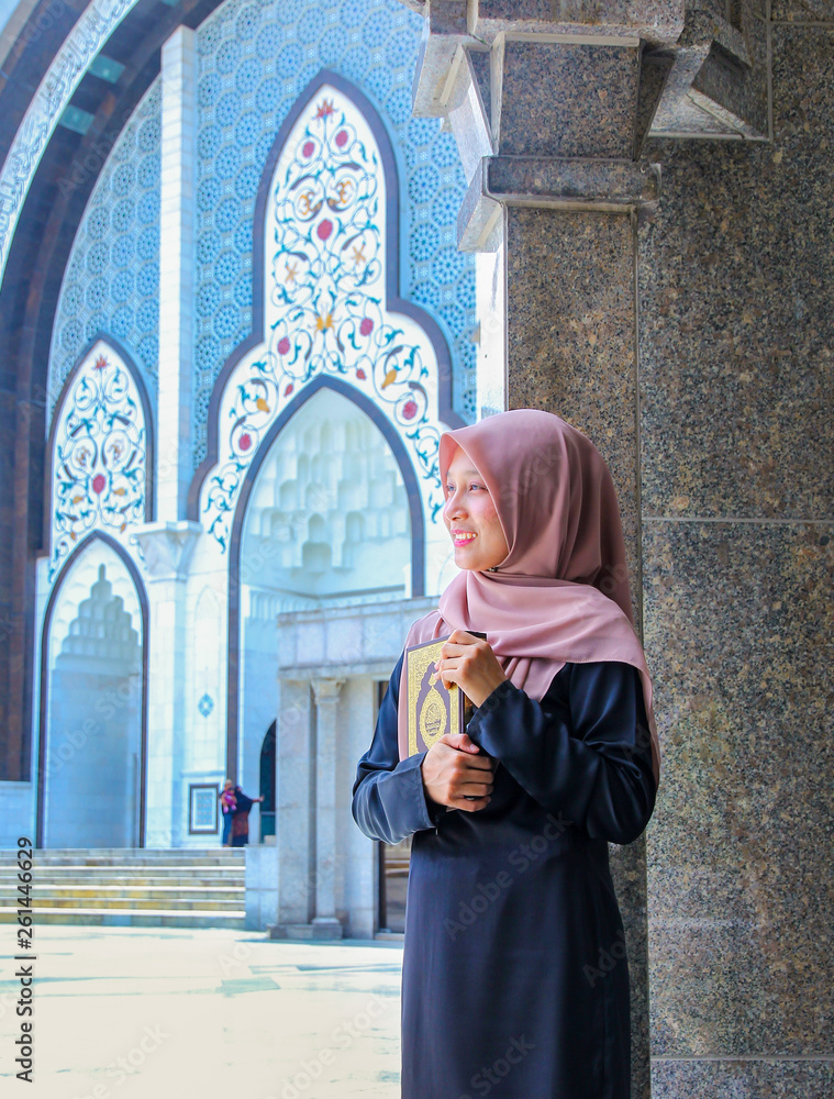 Young malay muslim women reading the holy quran while leaning on a pillar outside a mosque. Young malay muslim women reading the holy quran while leaning on a pillar outside a mosque.