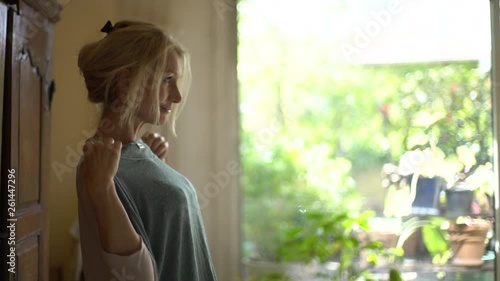 Medium shot of a mature woman standing in the bedroom holding top against her chest and smiling