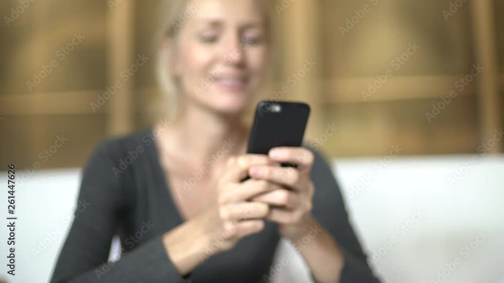 Rack focus of a smiling woman texting on her smart phone while sitting on a bed Rack focus of a smiling woman texting on her smart phone while sitting on a bed