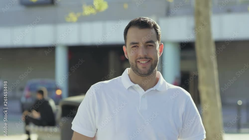 Smiling young man with hand on chin looking at camera. Handsome bearded brunet smiling and laughing. Happiness concept Smiling young man with hand on chin looking at camera. Handsome bearded brunet smiling and laughing. Happiness concept