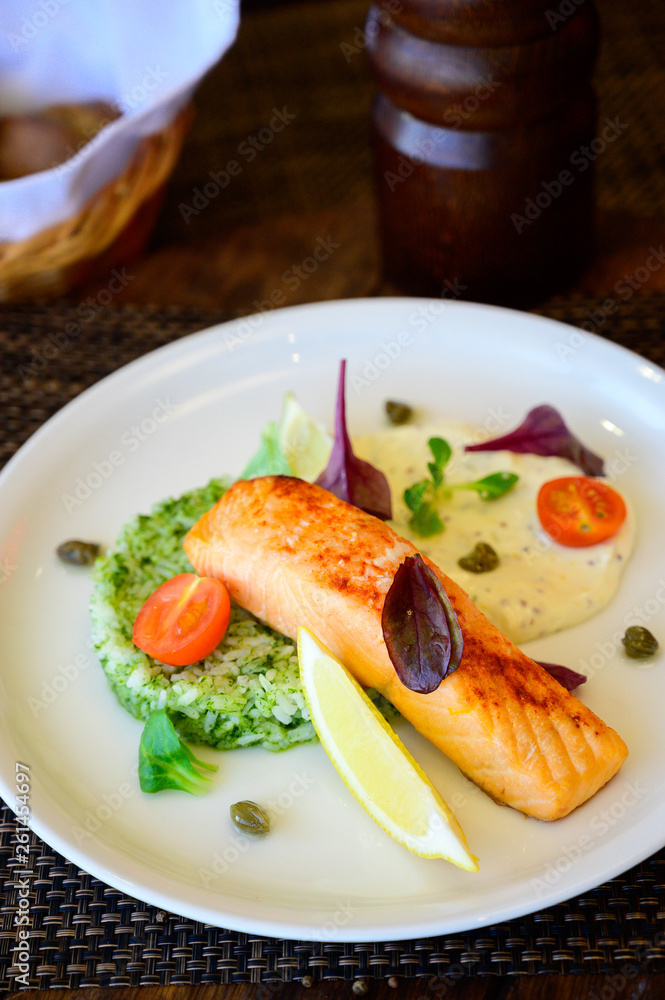 A piece of baked fish with lemon, vegetables and sauce A piece of baked fish with lemon, vegetables and sauce