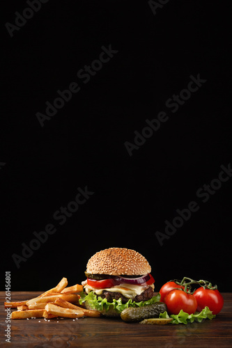 Homemade hamburger close-up with beef, tomato, lettuce, cheese and french fries on wooden table. Fastfood on dark background
