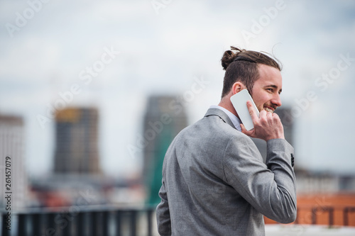 A young businessman with smartphone standing on a terrace, making a phone call.