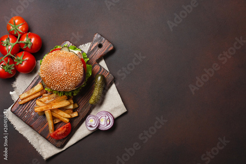 Homemade hamburger with ingredients beef, tomatos, lettuce, cheese, onion, cucumbers and french fries on cutting board and rusty background