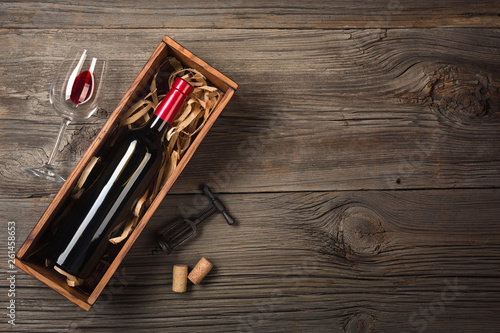 Red wine in a box with a glass and a corkscrew on a wooden table. Top view with space for your greetings