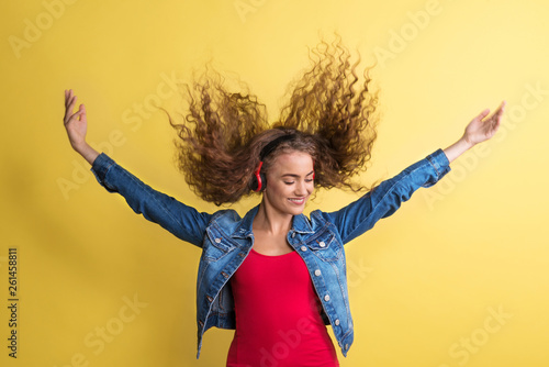 Portrait of a young woman with headphones in a studio on a yellow background.
