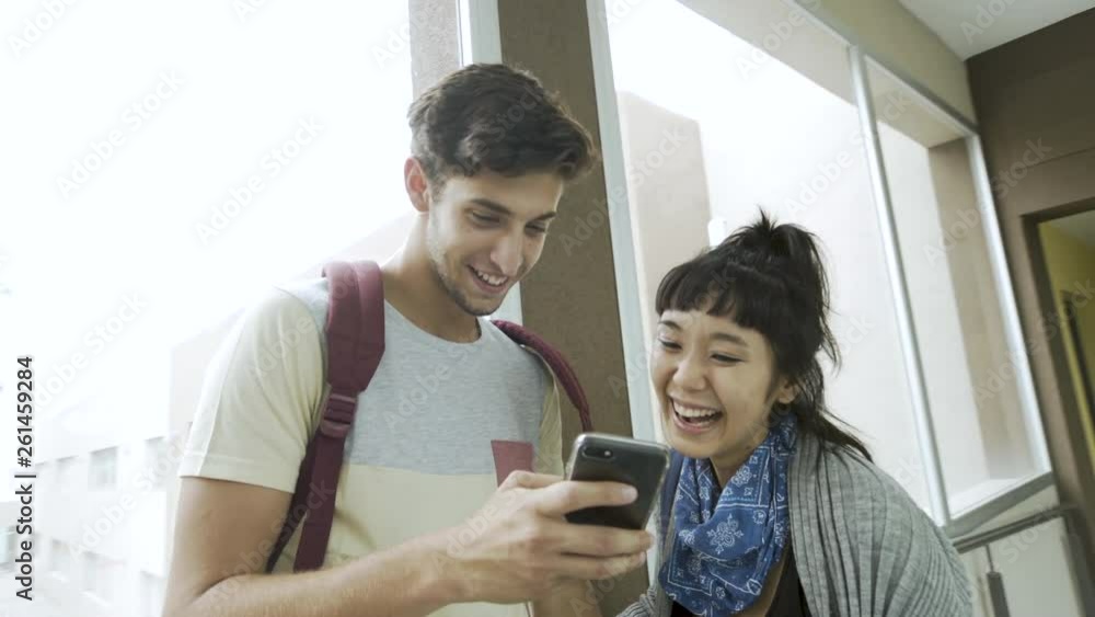 Medium shot of teenage students talking and using phone while sitting in college corridor Medium shot of teenage students talking and using phone while sitting in college corridor