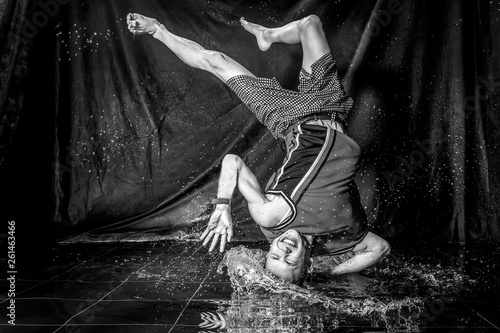 cool and happy korean young guy break dancer in style of bboying doing complex tricks on floor with water splashes and liquid drops effects in aqua zone photo studio with black isolated background