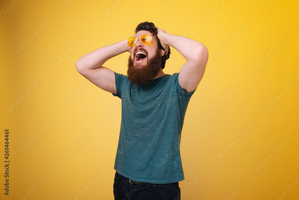 Screaming bearded man with hands on head, headache and suffering, isolated yellow background Screaming bearded man with hands on head, headache and suffering, isolated yellow background