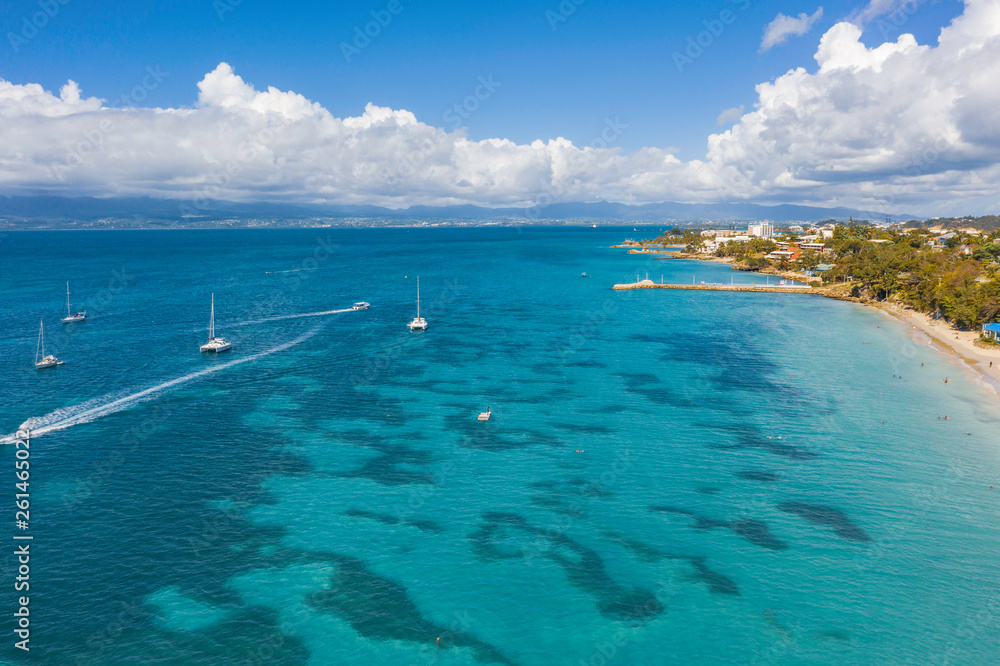 Scenic aerial view of La Datcha beach (Le Gosier plage) in Guadeloupe. Beautiful summer sunny look of small paradise tropical island in Caribbean sea. Several boats and yachts in blue sea.