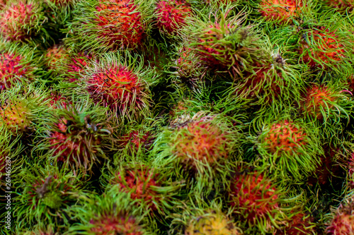 Pile of tropical rambutan fruits. Pink and spiky rambutan are piled on a table at a farmers market. Healthy fruits rambutans background. 