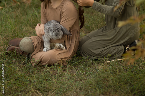 a gray rabbit is sleeping in the arms of a girl sitting on the grass.