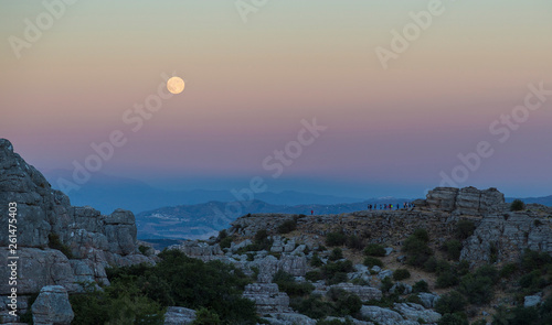 A big moon rising over the Torcal de Antequera in Spain and a group of people admiring it.