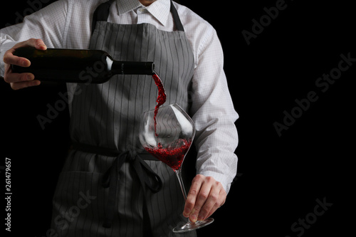 bartender pours wine in glass on dark background photo