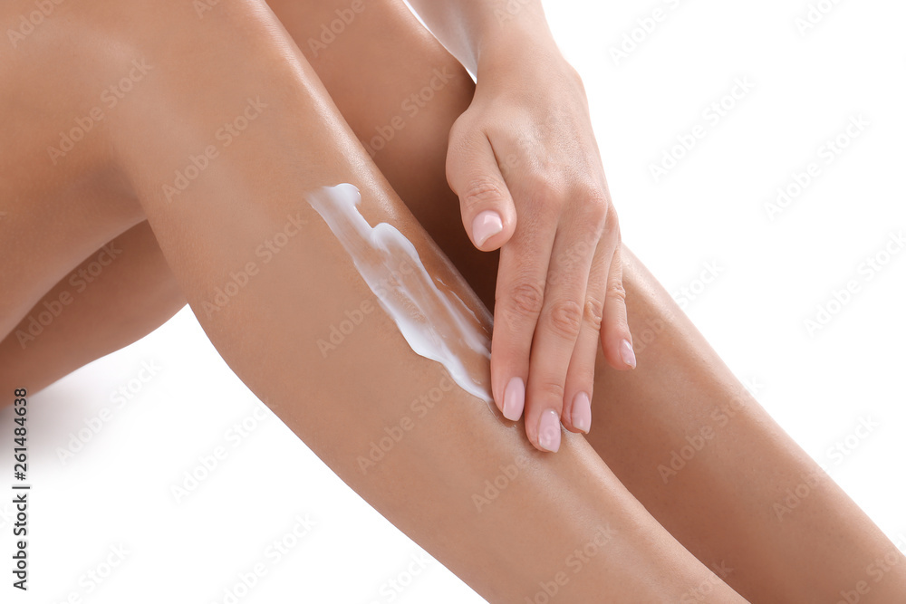 Fototapeta premium Young woman with perfect skin applying cream on white background, closeup of legs. Beauty and body care