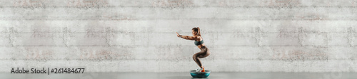 Side view of sporty woman doing exercises on bosu ball. In background gray wall, copy space.