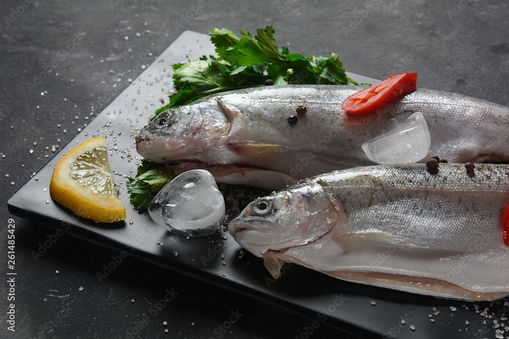 Fresh trout with salt, pepper, lemon on dark background 
