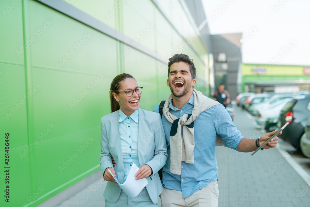 Happy laughing colleagues walking on the street. Woman holding paperwork and man holding tablet.