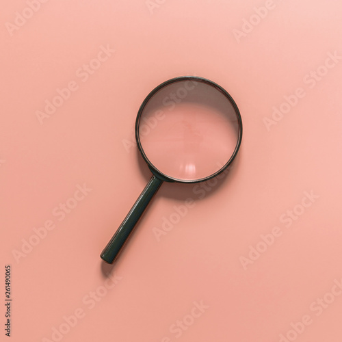 Black magnifying glass on a pink background. Copy space for text