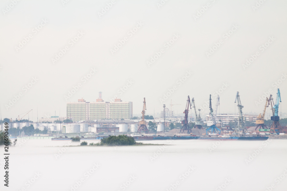 Cranes and industrial barges in the port, against a background of cloudy weather with fog in the summer. Russia, Krasnoyarsk.