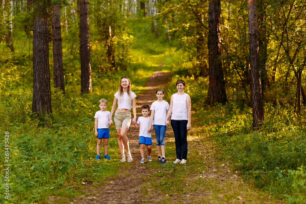 Fototapeta premium two women and three children walk through the forest, holding hands. in full growth summer