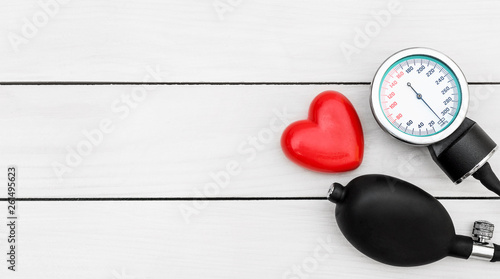 Manometer for measuring blood pressure with red heart on wooden background.