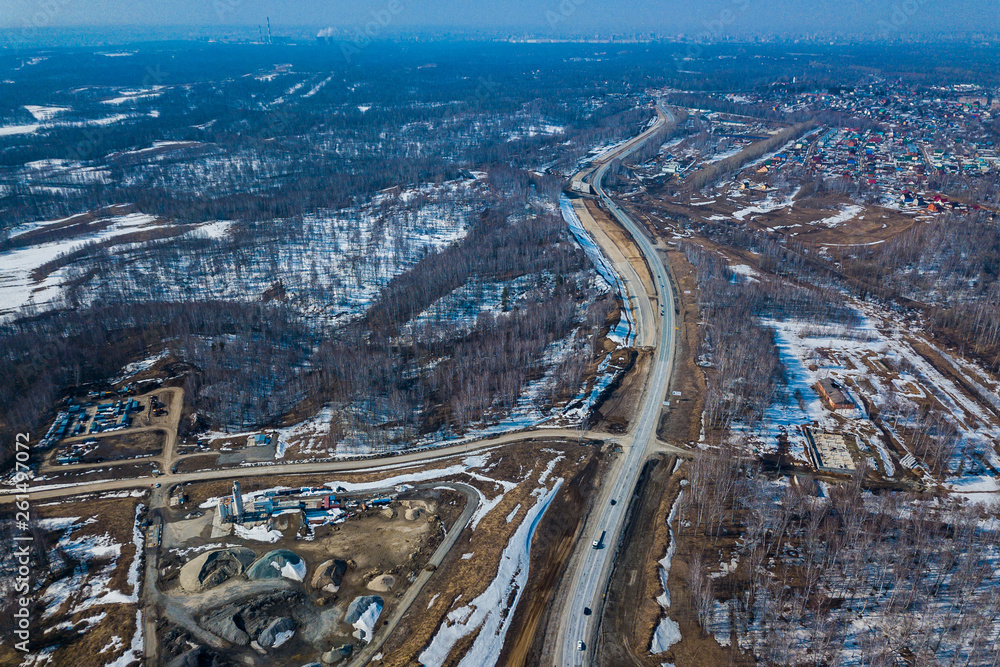 Helicopter drone shot. Aerial photography of a modern roads with car, track in winter, on background forest, construction site, no people