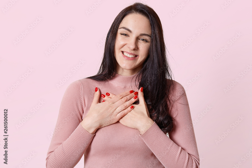 Adorable attractive young woman crosses hands on her chest, getting compliments, looks moving, wearing light pink jumper. People, communication and beauty concept. Copy space for advertisement. Adorable attractive young woman crosses hands on her chest, getting compliments, looks moving, wearing light pink jumper. People, communication and beauty concept. Copy space for advertisement.
