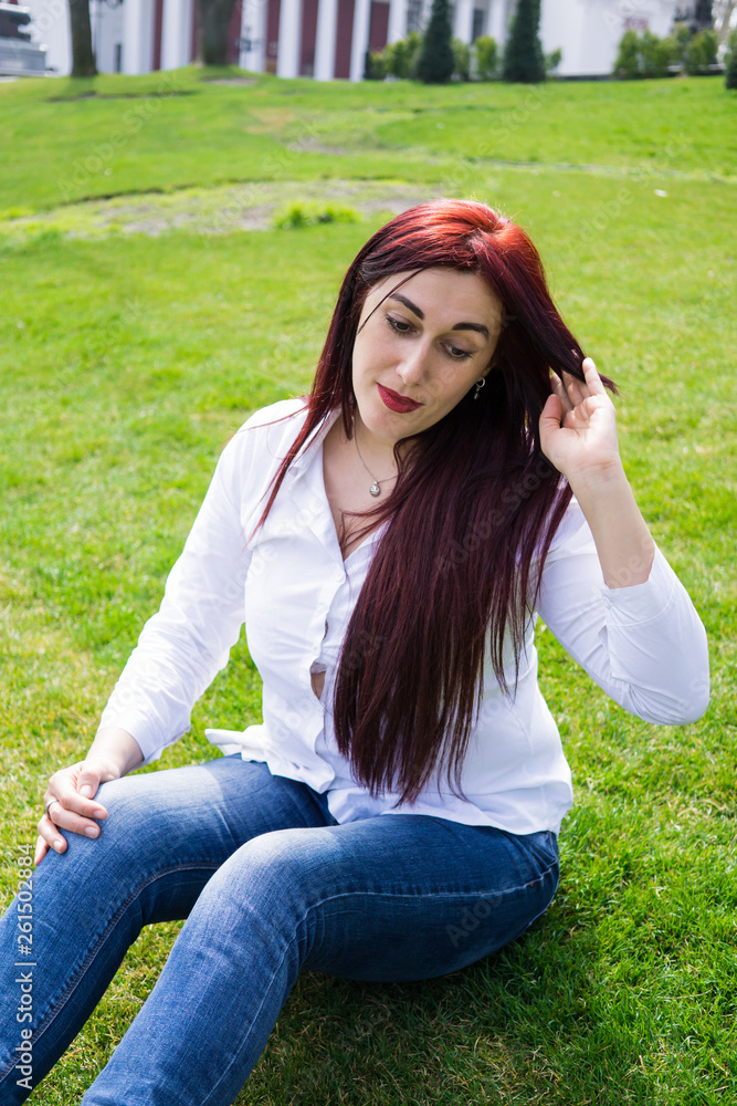 Young woman in white shirt and blue jeans sitting on a green grass
