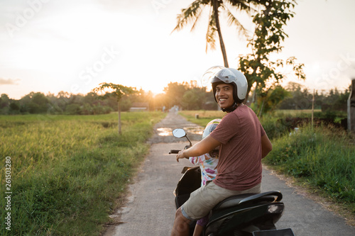 asian father and child look at sunset while riding motorbike scooter