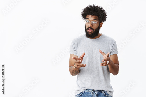 Handsome masculine bearded african american man in glasses with tattoos gesturing and waving hands as talking, explaining how product work raising eyebrows, describing thing to customer