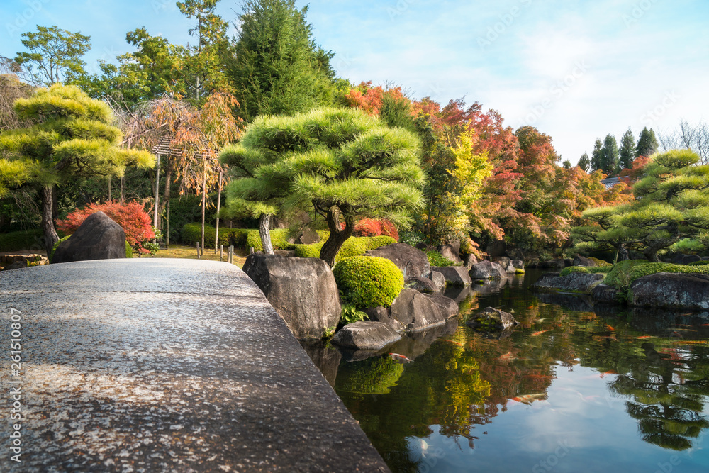 Low angle view from the stone bridge over the pond at Koko-en Gardens in Himeji, Japan - Sunny aspect of the park with colorful trees in autumn and Koi fish in the pond.