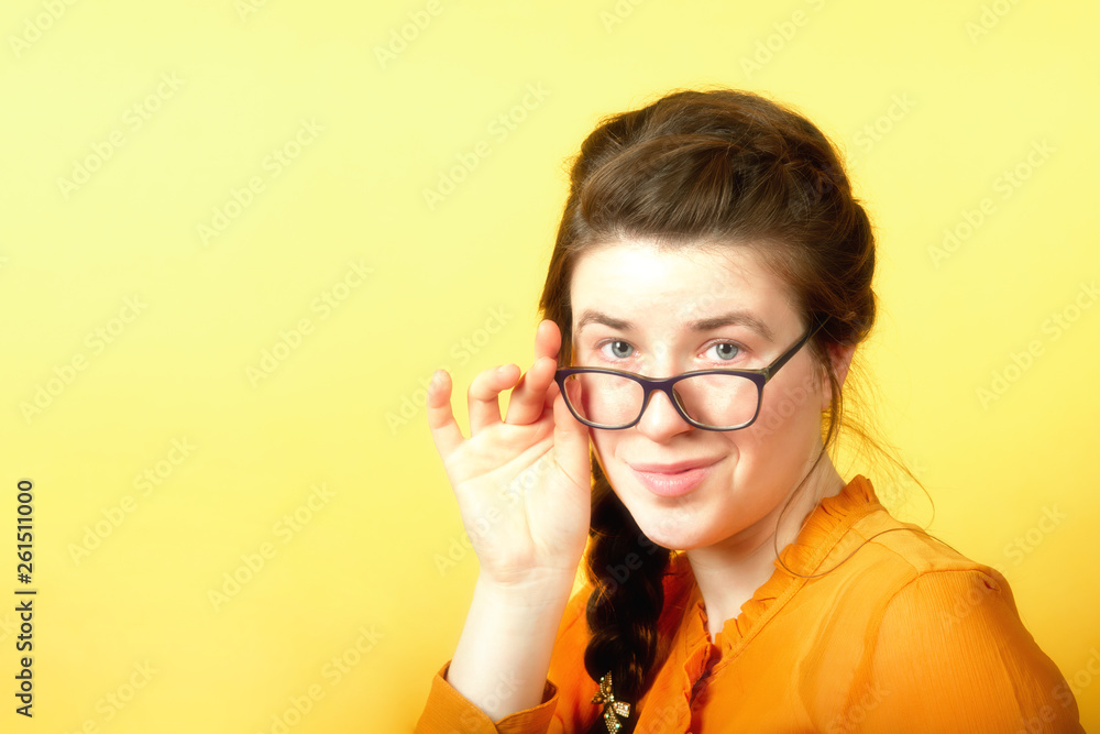 Girl holds glasses with hand on yellow background, concept of office employee about to leave.