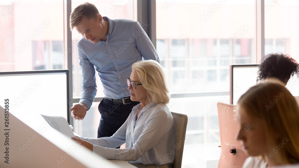 Serious manager mentor helping old employee with paperwork in office Serious manager mentor helping old employee with paperwork in office