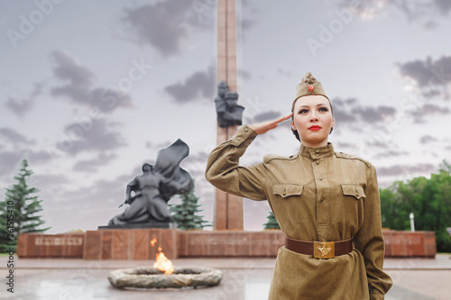 A girl in an old Soviet military uniform salute near the eternal flame. The celebration and commemoration of the Second World War on May 9 photo