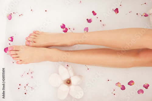 Woman is taking bath. Close up of female feet and hands in bath full of water and flowers.