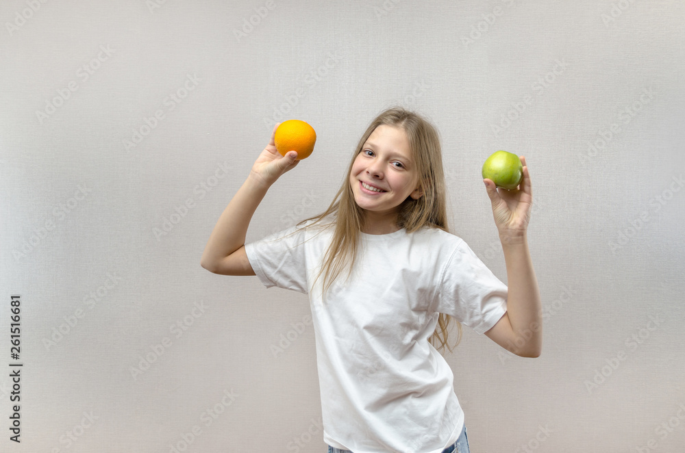 Beautiful blonde girl in a white T-shirt smiles and holds an apple and an orange in her hands. Healthy nutrition for schoolchildren. Useful fruits for children's health. Health care