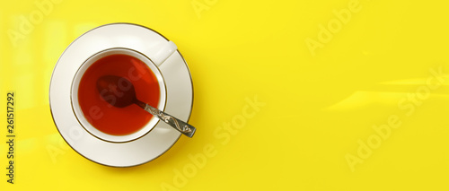 Flat lay photo - white porcelain cup with spoon filled hot amber tea, on yellow board, wide banner space for text right