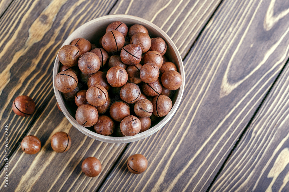 Obraz premium Macadamia nuts in bowl on a wooden table with copy space. Top wiew.