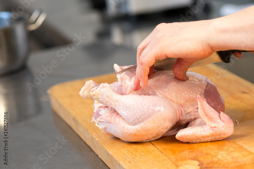 A person cuts raw chicken. Cook's hand with a knife close-up on the background of the kitchen