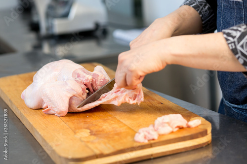 A person cuts raw chicken. Cook's hand with a knife close-up on the background of the kitchen.