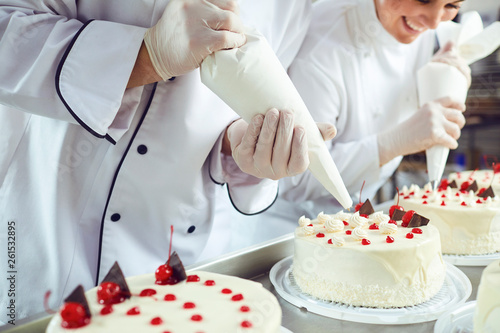 Two pastry chefs decorate a cake from a bag in a pastry shop photo